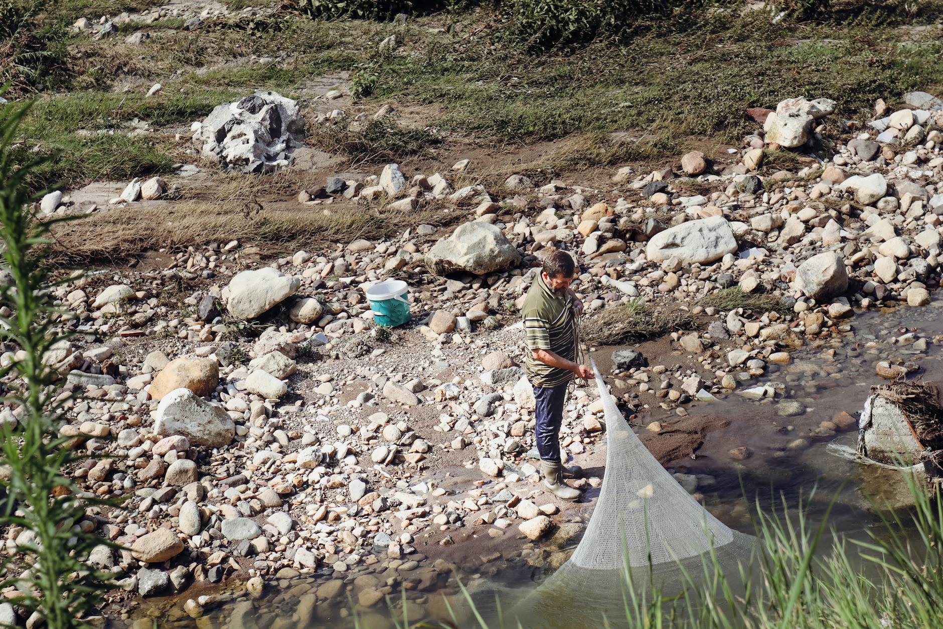 Mężczyzna brodzący w płytkiej, kamienistej rzece z siatką do połowu