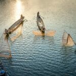 Rybacy w łodziach zarzucający sieci o zachodzie słońca