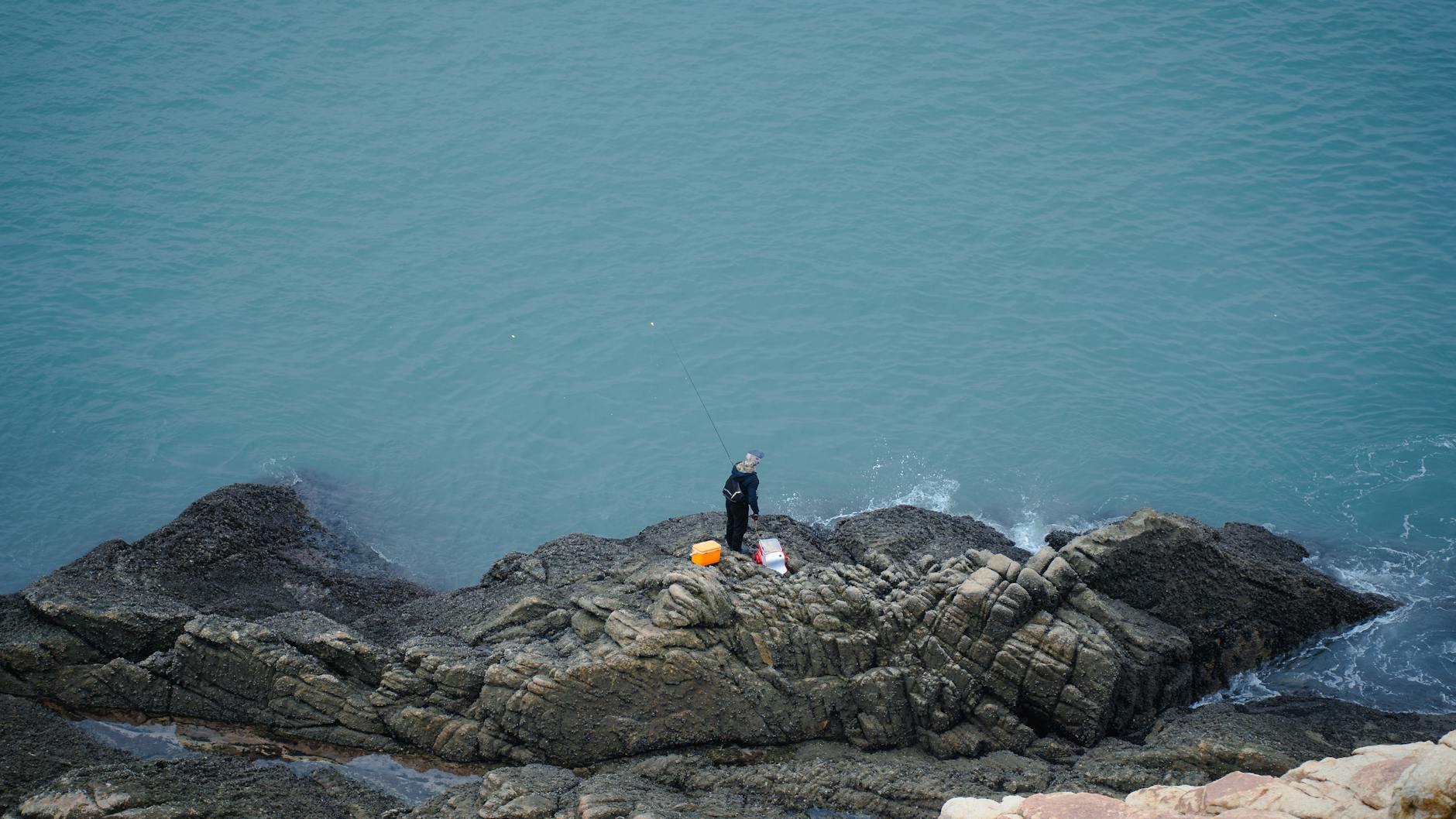 Wędkarz samotnie łowiący z kamienistego brzegu nad wodą