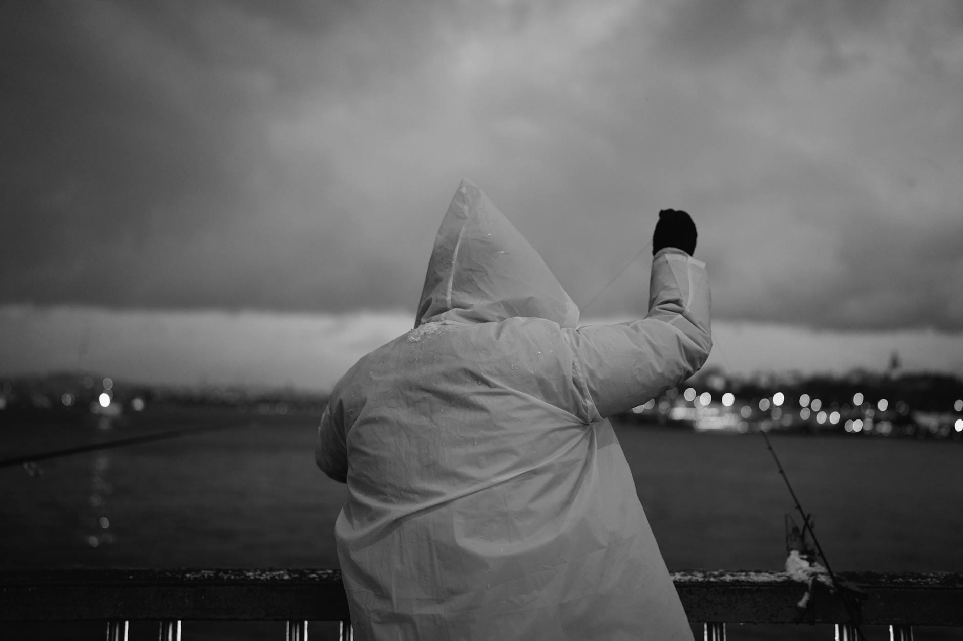 Wędkarz w kapturze łowiący w deszczu przy wzburzonym morzu o zmierzchu