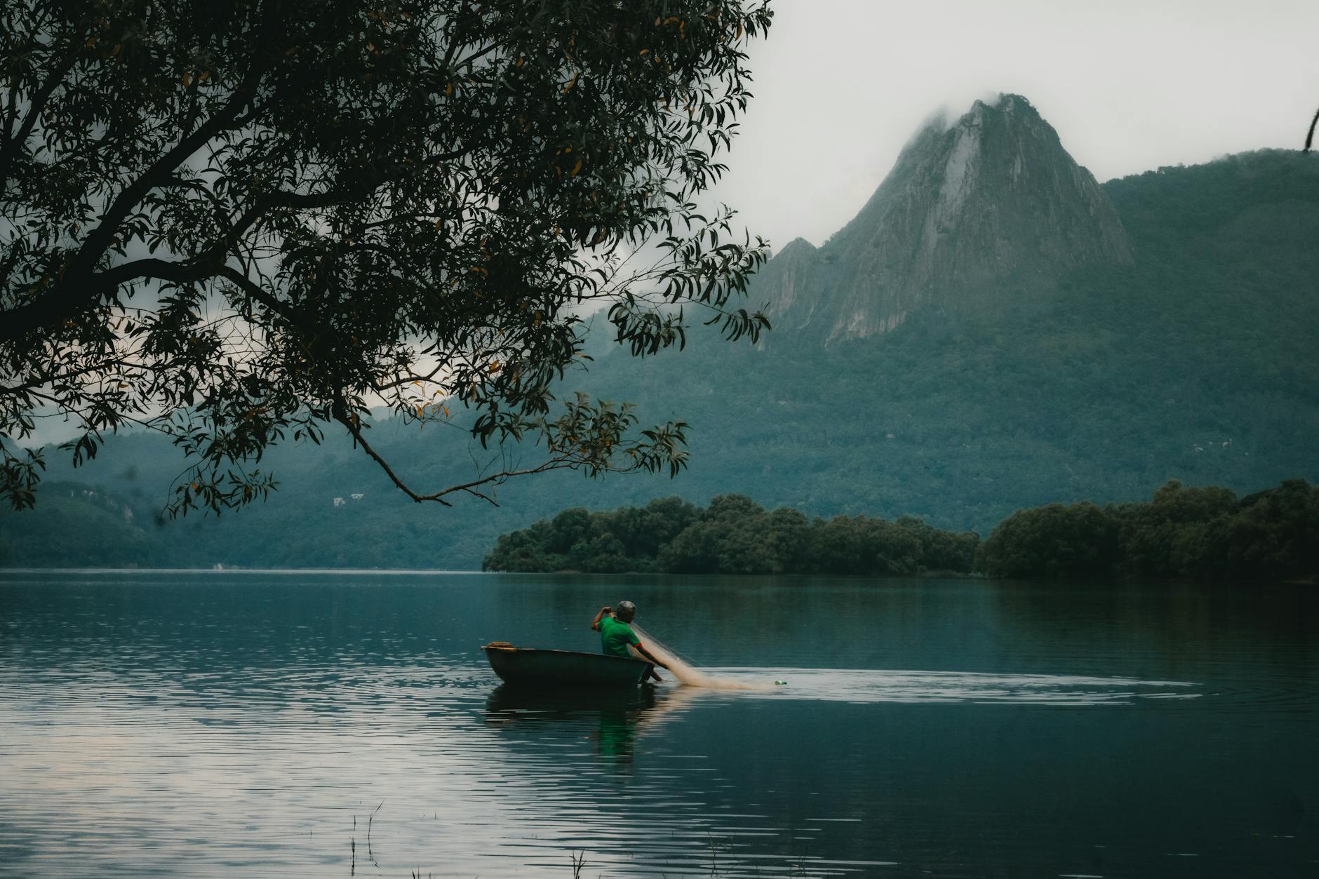 Wędkarz zarzuca sieć z łodzi na spokojnym jeziorze wśród gór