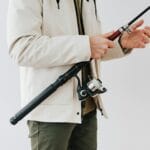 Początkujący wędkarz w kurtce trzymający wędkę i sprzęt nad wodą