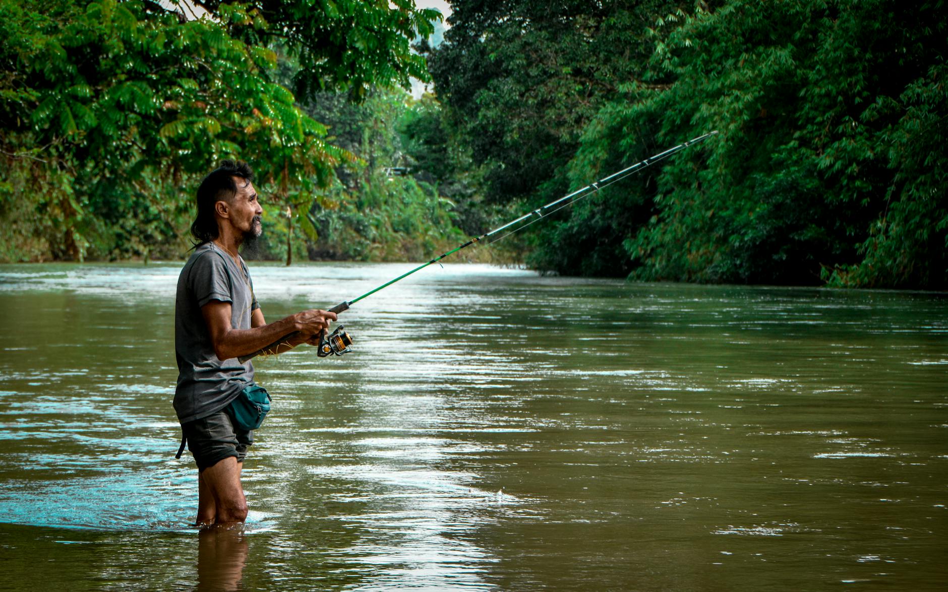 Wędkarz łowiący w spokojnej rzece otoczonej zielonym lasem