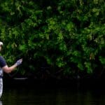 Wędkarz muchowy stojący w rzece otoczonej zielenią