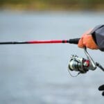 Wędkarz trzyma wędkę nad spokojnym jeziorem o świcie